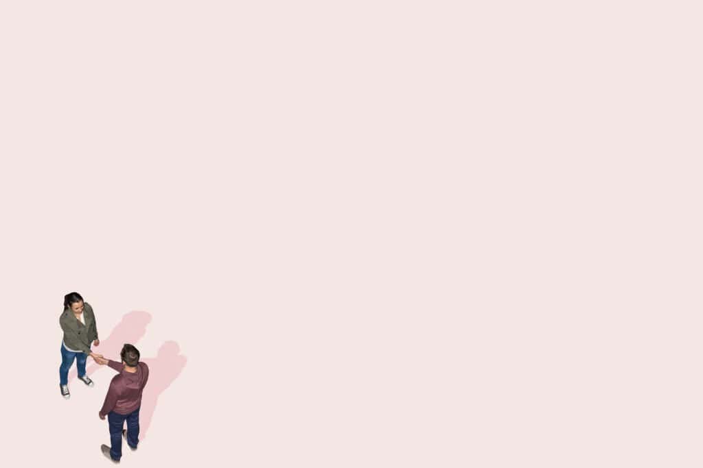 Aerial view of two people standing on a pale pink background, facing each other and shaking hands, with plenty of empty space around them. | sjhstudios