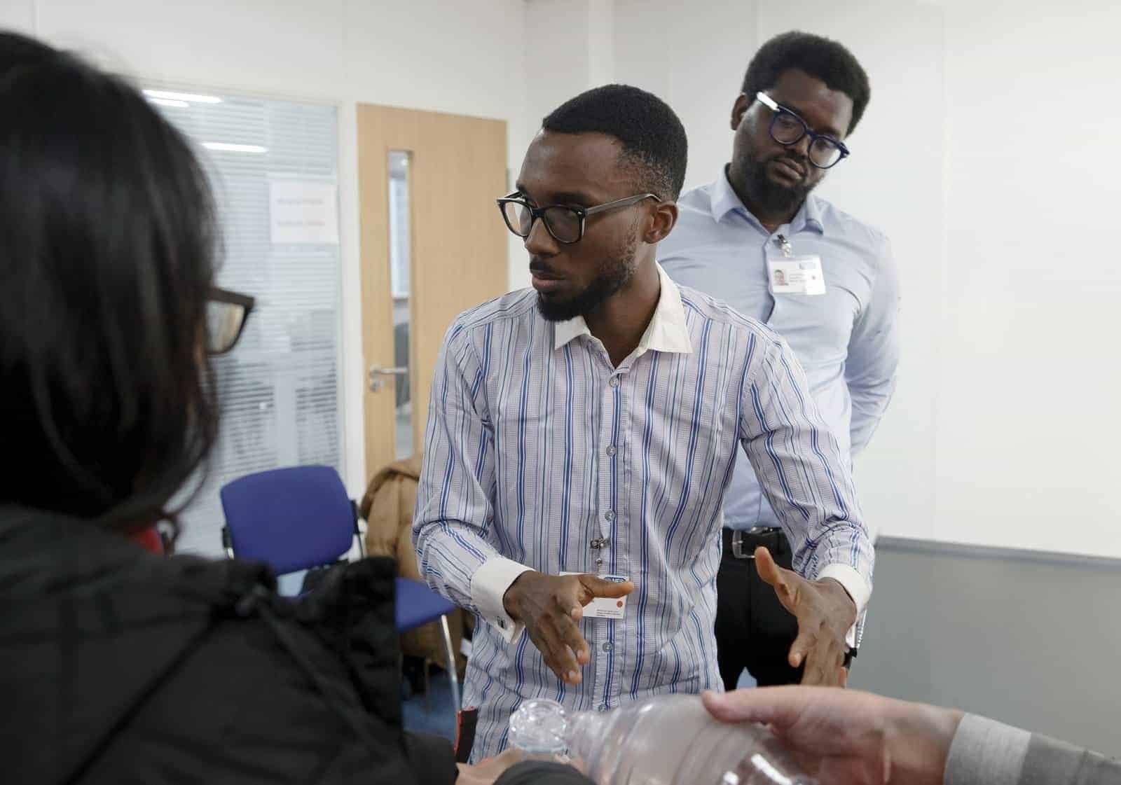 Two men wearing glasses and business attire are having a serious conversation with a woman in an office setting. One man gestures with his hands while the other listens attentively in the background. | sjhstudios
