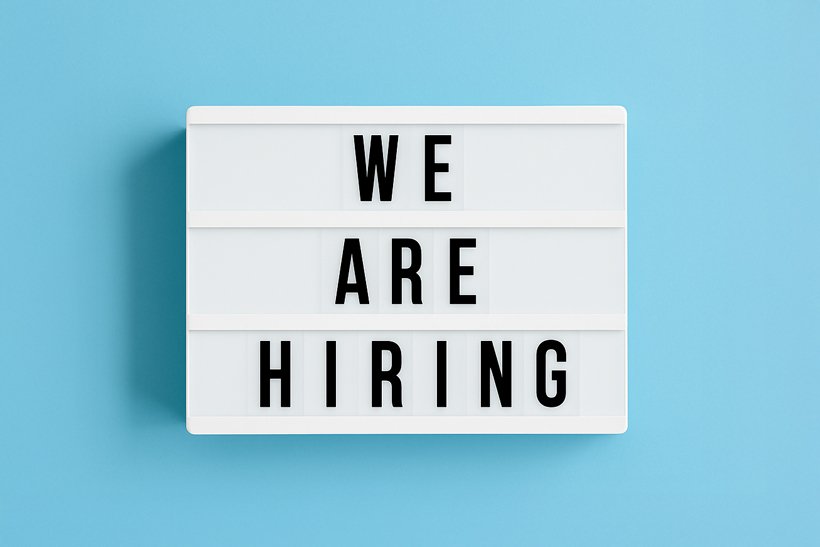 A white lightbox sign with black letters displays the message "WE ARE HIRING" against a light blue background. | sjhstudios